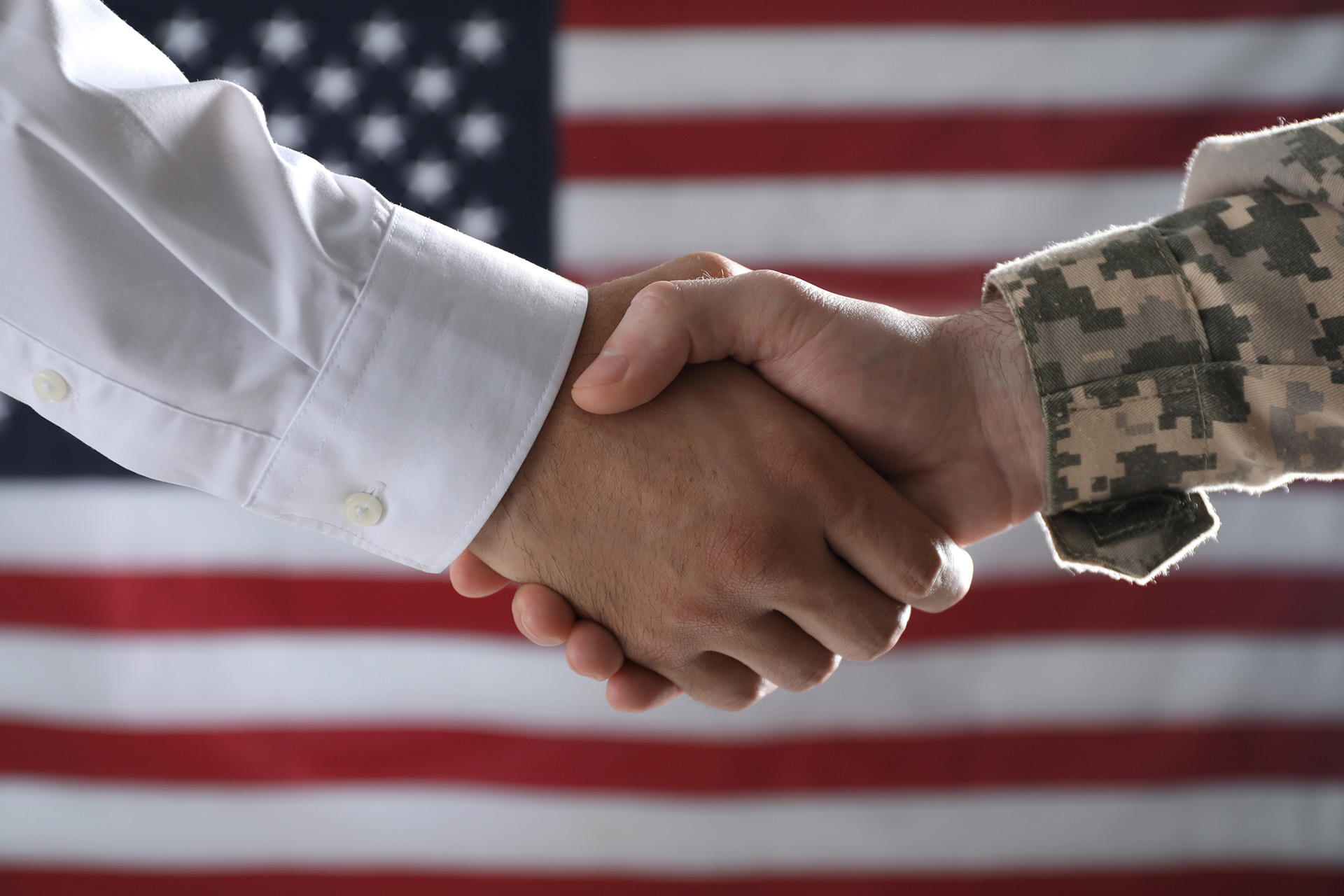 A veteran and a civilian shaking hands in front of a flag
