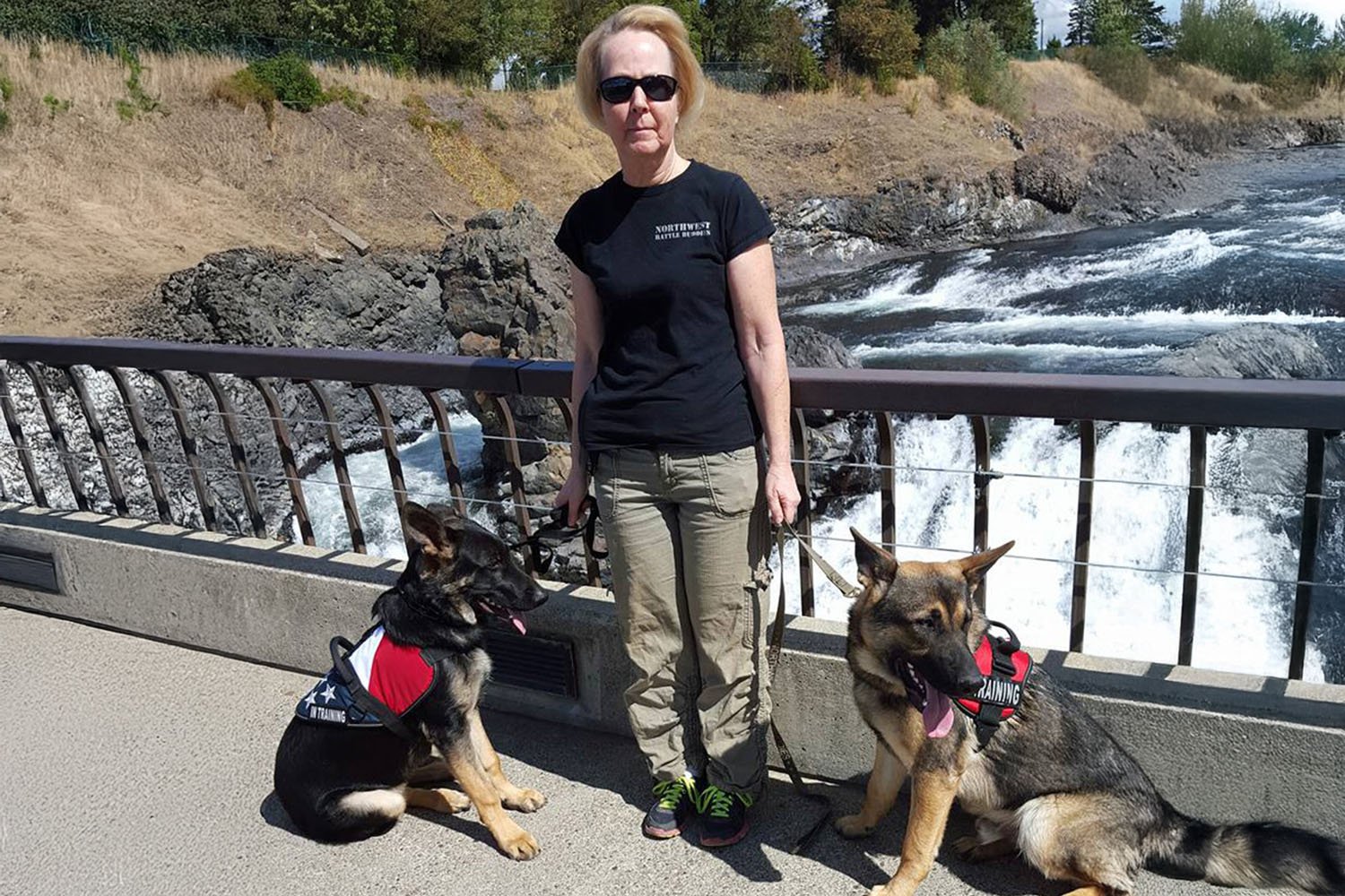 Dorothy poses on a bridge over a river with two service dogs