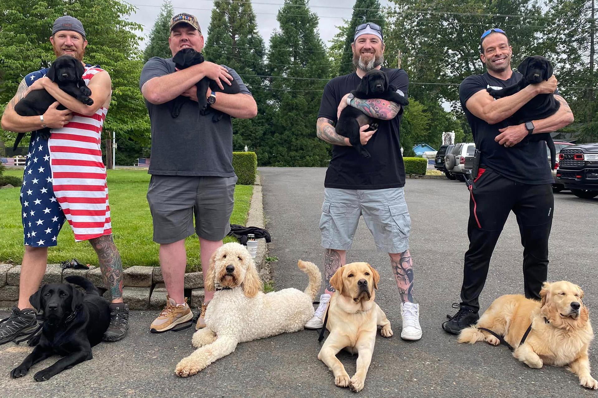 Veterans holding new service puppies, with older service dogs at their feet. 